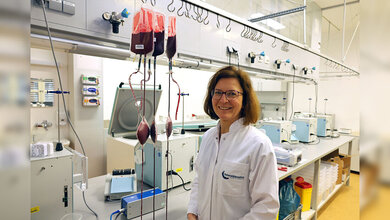 Forscherin im Labor in weißem Kittel vor Geräten und drei Blutkonserven.