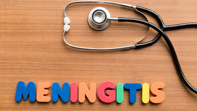 Buchstaben, die das Wort Meningitis bilden und ein Stethoskop auf einem Tisch.