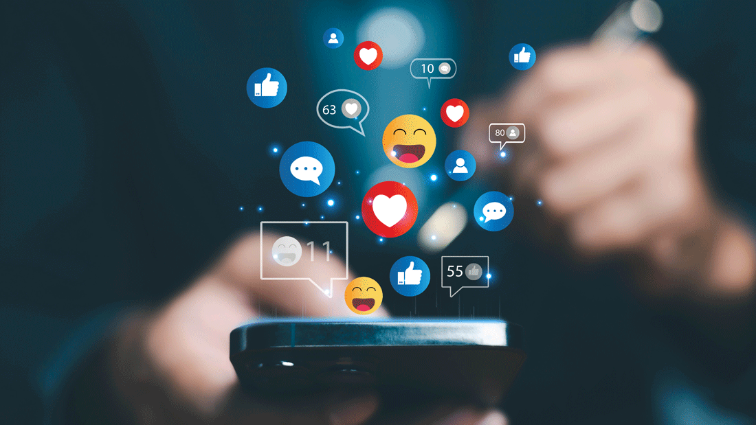 Das Bild zeigt eine Person, die ein Smartphone benutzt, während Symbole für soziale Interaktionen wie Likes, Kommentare und Emojis darüber schweben. 
