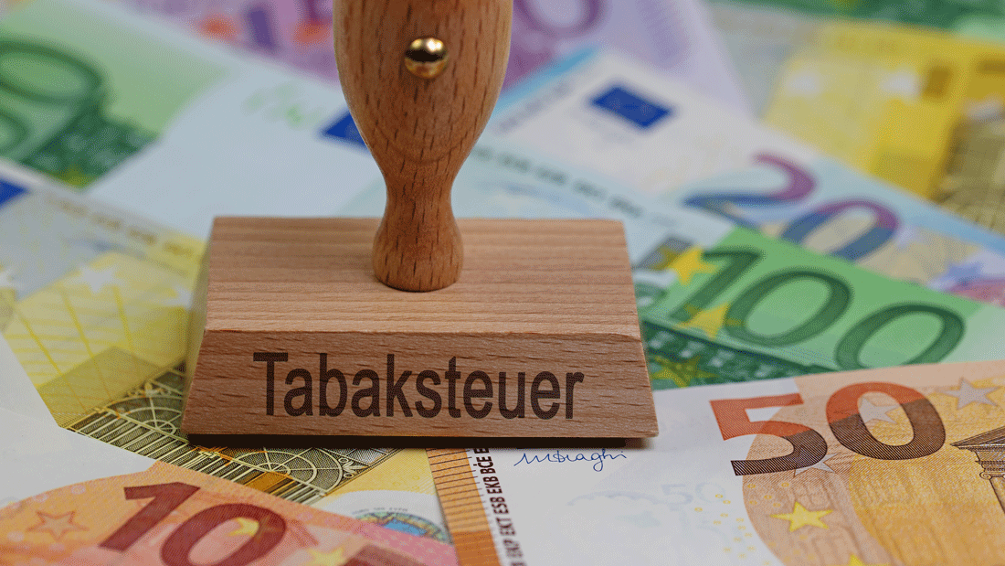 Holzstempel mit der Aufschrift „Tabaksteuer“ liegt auf Euro-Banknoten.