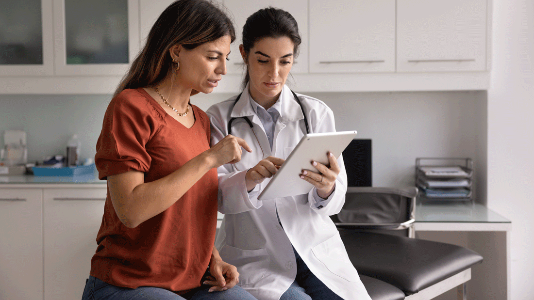 Patientin und Ärztin betrachten gemeinsam ein Tablet in einer Praxis.
