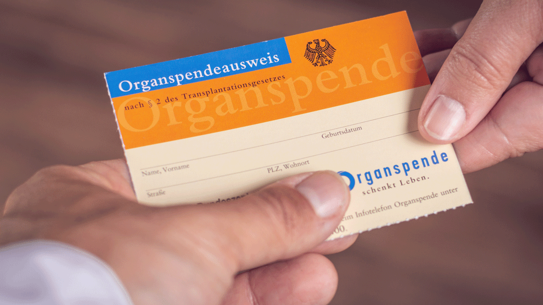 Das Bild zeigt einen deutschen Organspendeausweis, der von einer Person übergeben wird.
