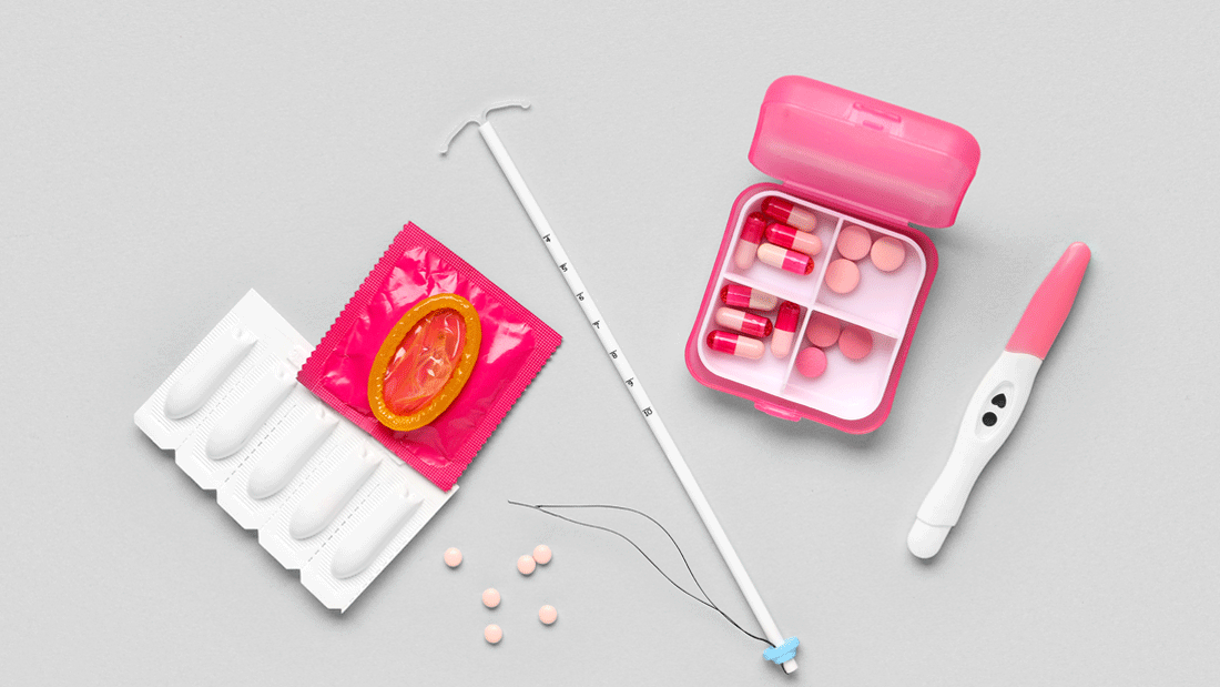Auf grauem Hintergrund liegen Verhütungsmittel: Spirale, Kondom, Vaginalzäpfchen, Pillendose mit Tabletten und ein positiver Schwangerschaftstest.