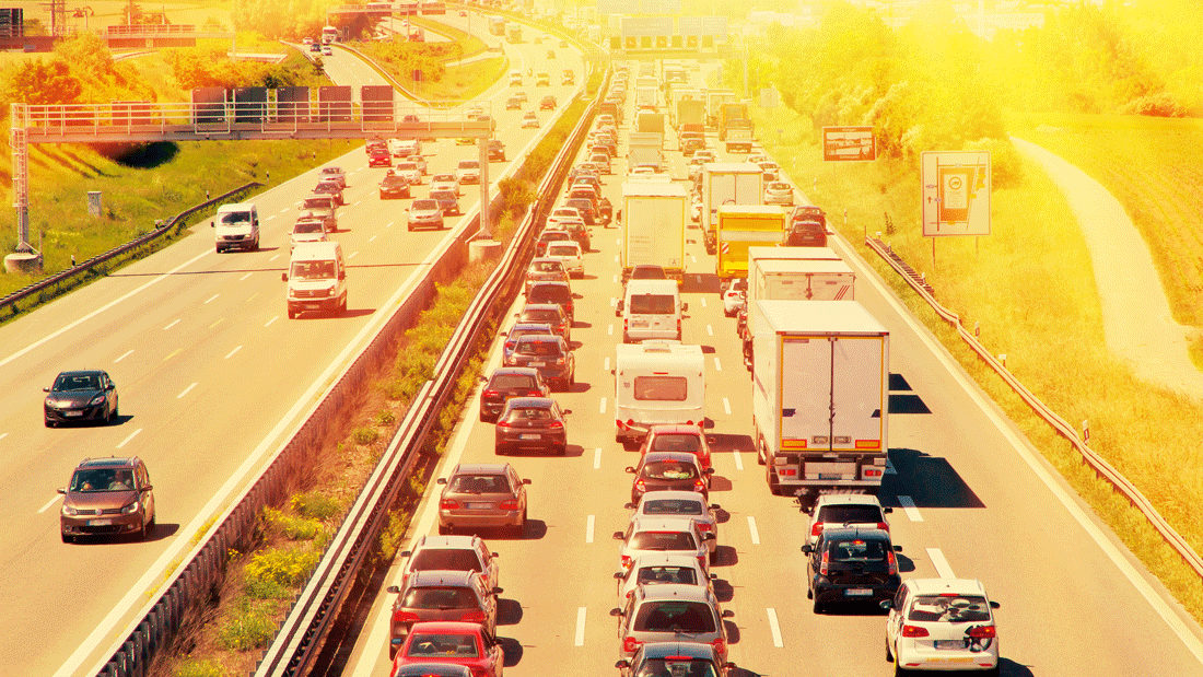 Das Bild zeigt eine stark befahrene Autobahn mit dichtem Verkehr, einschließlich Autos und Lastwagen, unter strahlendem Sonnenschein. Es könnte Themen wie Verkehrsstaus, Umweltbelastung, Mobilität oder Reiseplanung symbolisieren.