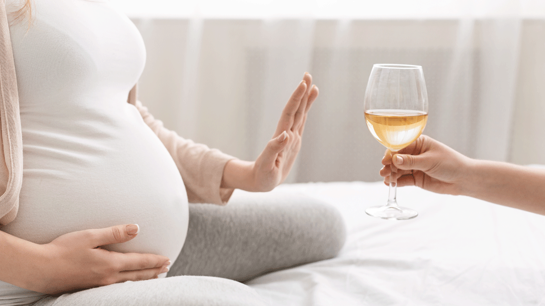  Das Bild zeigt eine schwangere Frau, die mit einer Hand ihren Bauch hält und mit der anderen Hand ablehnend ein Glas Wein zurückweist. Es symbolisiert die wichtige Botschaft, während der Schwangerschaft auf Alkohol zu verzichten, um die Gesundheit des ungeborenen Kindes zu schützen.