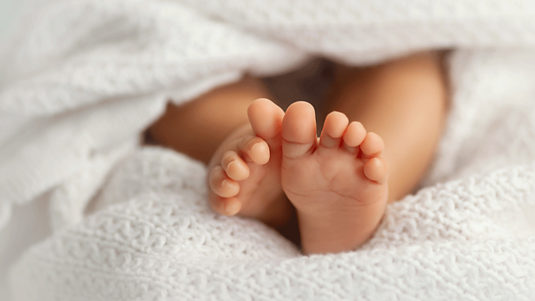 Nahaufnahme kleiner Babyfüße, die unter einer weichen weißen Decke hervorschauen