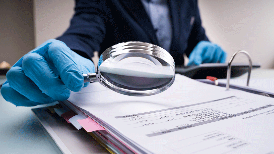 Dieses Bild zeigt eine Person, die mit einer Lupe Dokumente untersucht. Die Person trägt blaue Handschuhe, was auf eine sorgfältige oder professionelle Prüfung hinweisen könnte.