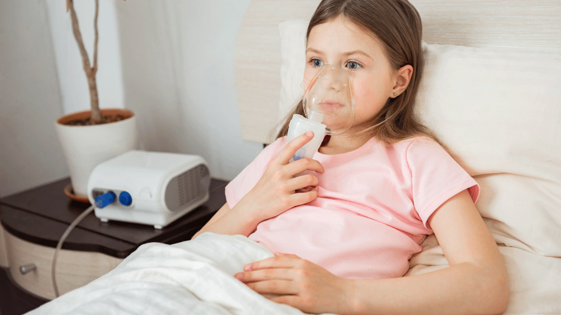 Dieses Bild zeigt eine junge Person, die im Bett liegt und einen Vernebler benutzt. Das Gerät steht auf einem Nachttisch, und die Person scheint über den Vernebler ein Medikament zu inhalieren.