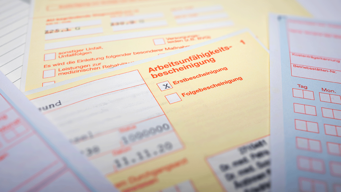 Mehrere gelbe Formulare zur Arbeitsunfähigkeitsbescheinigung liegen übereinander. Markiert ist eine Erstbescheinigung.