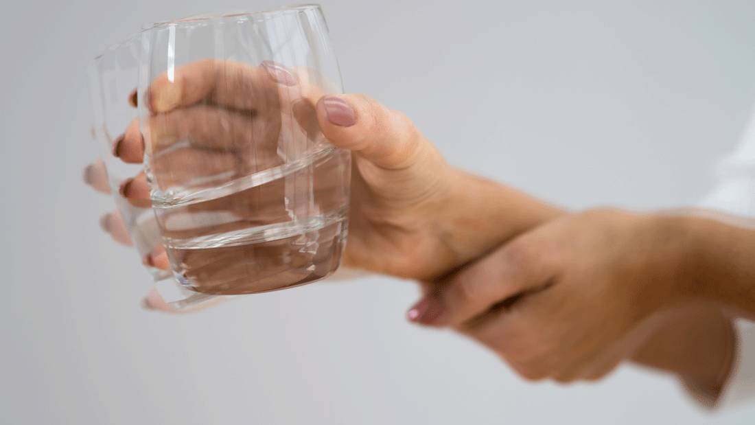AdobeStock_480511495.gif Das Bild zeigt eine Hand, die ein Glas Wasser hält, wobei die Bewegung der Hand durch eine Unschärfe oder Doppelung dargestellt wird. Dies könnte auf ein Zittern oder eine motorische Beeinträchtigung hinweisen.