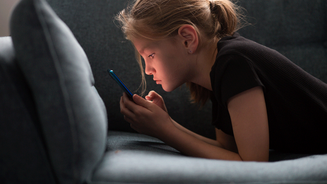 Das Bild zeigt ein Mädchen, das auf einem Sofa liegt und ein Smartphone benutzt.