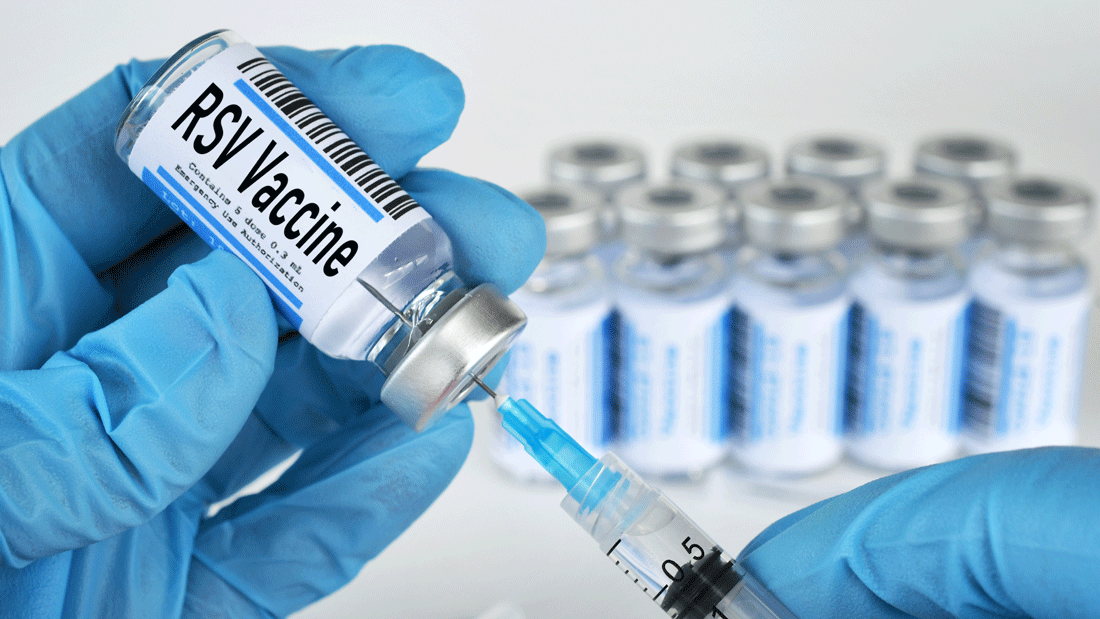 Das Bild zeigt ein Fläschchen mit der Aufschrift „RSV Vaccine", aus dem mit einer Spritze eine Dosis aufgezogen wird. Die Person trägt blaue medizinische Handschuhe. 