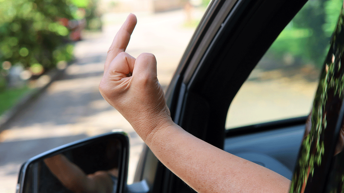 Das Bild zeigt eine Person, die aus einem Autofenster den Mittelfinger zeigt.