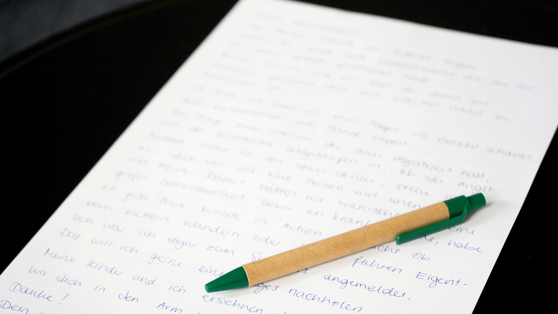 Handgeschriebener Brief auf weißem Papier mit grünem Kugelschreiber auf dunkler Unterlage