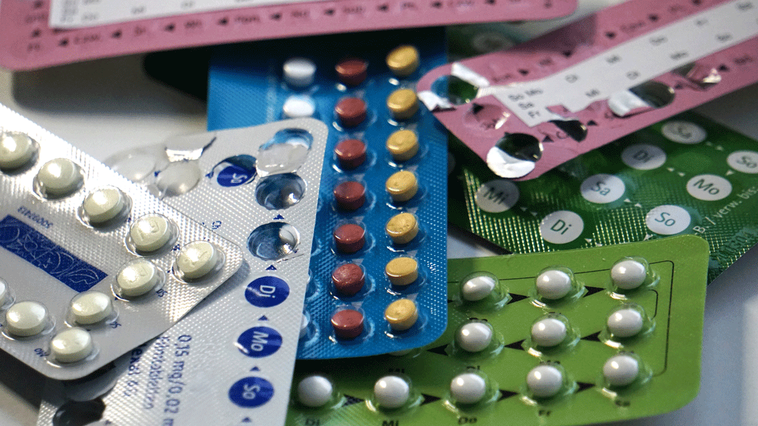 Mehrere bunte Blisterpackungen mit Antibabypillen liegen übereinander. Sichtbar sind Wochentage und unterschiedliche Tablettenfarben.